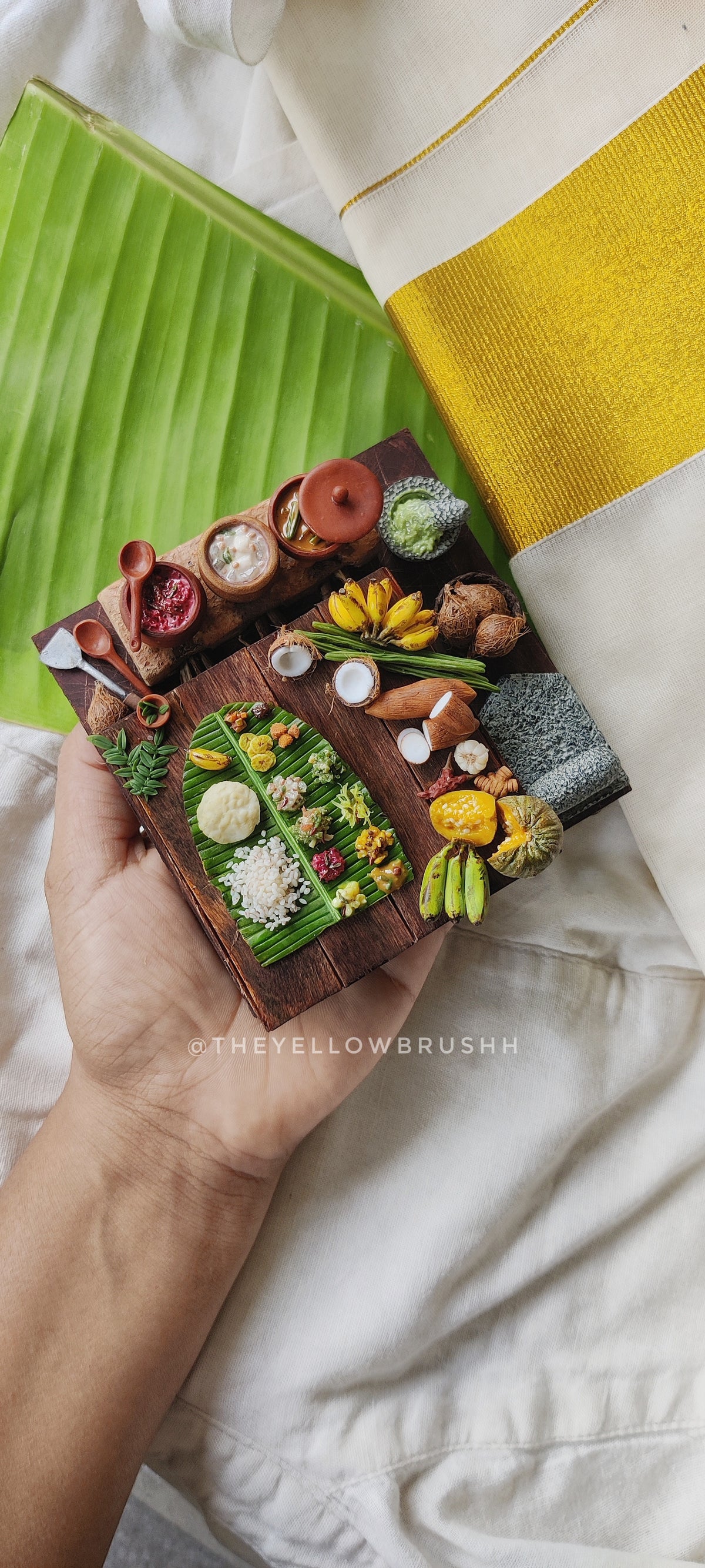 Miniature Onam festival feast display with banana leaves, fruits, coconuts, and serving bowls